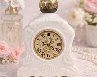 May include: A white ceramic mantel clock with a gold-coloured top. The clock face displays Roman numerals and floral details. The clock has an ornate, vintage design, with decorative swirls and a classic aesthetic.