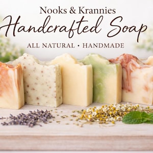 May include: Handcrafted soap bars in various colors and textures, with the text "Nooks & Krannies Handcrafted Soap, All Natural, Handmade." The soaps are arranged on a wooden surface with herbs and flowers.