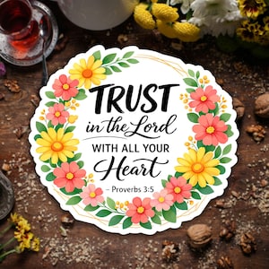 May include: A round sticker with a floral wreath design. The sticker features the text "TRUST in the Lord WITH ALL YOUR HEART - Proverbs 3:5" in black script. The wreath includes yellow, pink, and red flowers with green leaves.