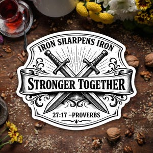 May include: A black and white sticker with the text "Iron Sharpens Iron" and "Stronger Together" with crossed swords. The sticker also includes the Bible verse "27:17 - Proverbs". The design is surrounded by decorative flourishes.