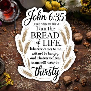 May include: A white sticker with the text "John 6:35" and "I am the bread of life." The sticker has wheat stalks and a decorative border. The background is a wooden surface with walnuts and flowers.