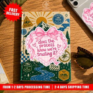 May include: A rectangular notebook featuring a mountain landscape illustration with a sun, river, and various adventure-themed badges. A large pink heart-shaped sticker with a bow and the text does the process know we're trusting it? is centered.