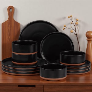 May include: A black ceramic dinnerware set with a rustic design. The set includes plates, bowls, and serving dishes with a contrasting terracotta-colored rim. A wooden cutting board and decorative sprig are also present.