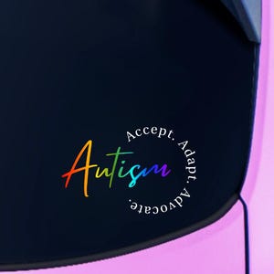 May include: A rainbow-colored "Autism" decal with the words "Accept. Adapt. Advocate." in a circular design. The sticker is affixed to the rear window of a pink vehicle, with the car's taillight visible.