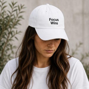 Peut inclure: Casquette de baseball blanche avec le texte "Focus Wins" en noir. La casquette est faite d'une matière douce et possède une visière incurvée. Le chapeau est de style classique, adapté aux tenues décontractées.