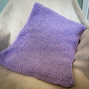 May include: A soft, plush, lavender-colored blanket. The blanket has a gradient effect, transitioning from a darker shade of purple to a lighter shade. The texture appears to be a knitted or crocheted design, creating a cozy and inviting appearance.