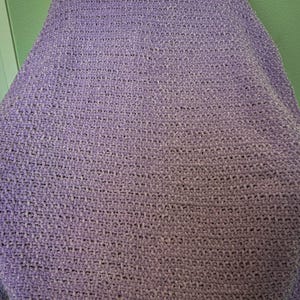 May include: A soft, lavender-colored blanket. The blanket is made of a plush, textured material, likely knitted or crocheted. The color is a light purple, with variations in tone across the surface.