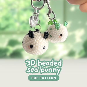 May include: Two 3D beaded sea bunny charms crafted from small white beads. One features black accents and the other green accents, both with tiny black eyes and pink cheeks. They hang from silver-toned metal clasps. Text reads 3D beaded sea bunny PDF PATTERN.