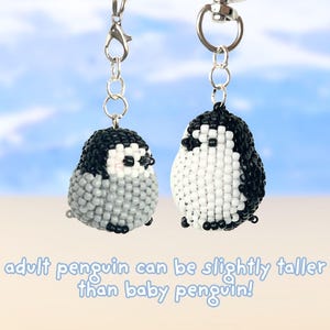 May include: Two beaded penguin keychains with silver-tone metal clasps. The left penguin is grey and white, while the right penguin is black and white. The text below reads: adult penguin can be slightly taller than baby penguin!