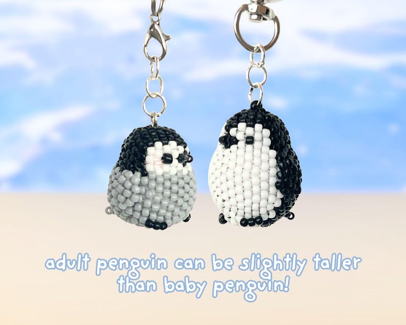 May include: Two beaded penguin keychains with silver-tone metal clasps. The left penguin is grey and white, while the right penguin is black and white. The text below reads: adult penguin can be slightly taller than baby penguin!