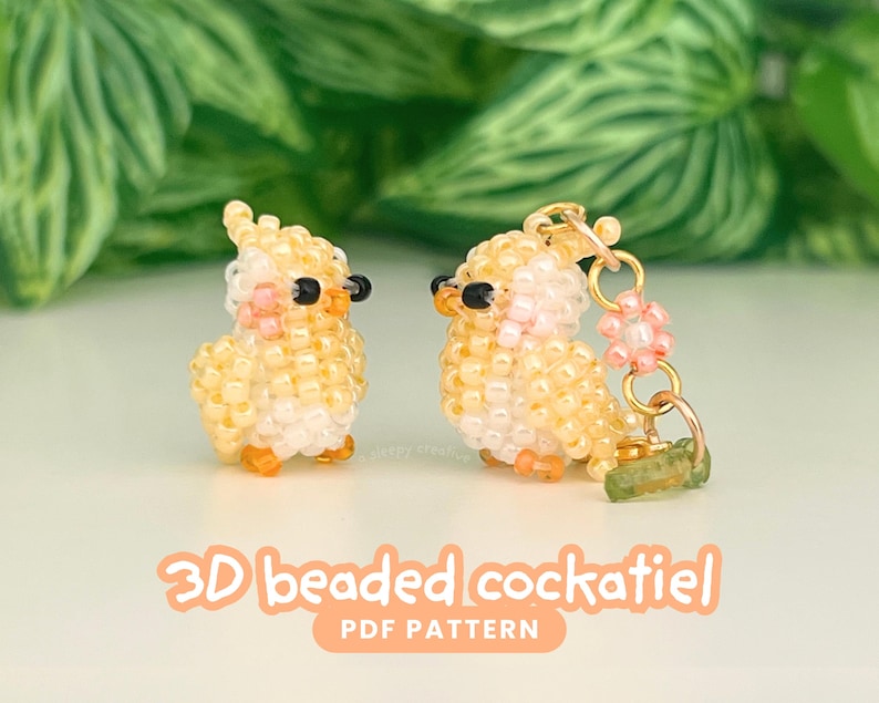 May include: Two 3D beaded cockatiel figures crafted from small yellow, white, and pink beads with black bead eyes and orange accents. One figure is a standalone ornament, while the other is attached to a gold-toned metal ring with a small flower charm.