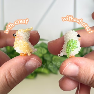 May include: Two miniature bird figurines crafted from small beads. The left bird is yellow and white with a crest, labeled 'with crest'. The right bird is white with green wing details and no crest, labeled 'without crest'. Both have black eyes.