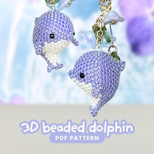May include: Two beaded dolphin ornaments in shades of purple and white, suspended from gold-coloured chains with floral accents. The text "3D beaded dolphin PDF PATTERN" is displayed at the bottom of the image.