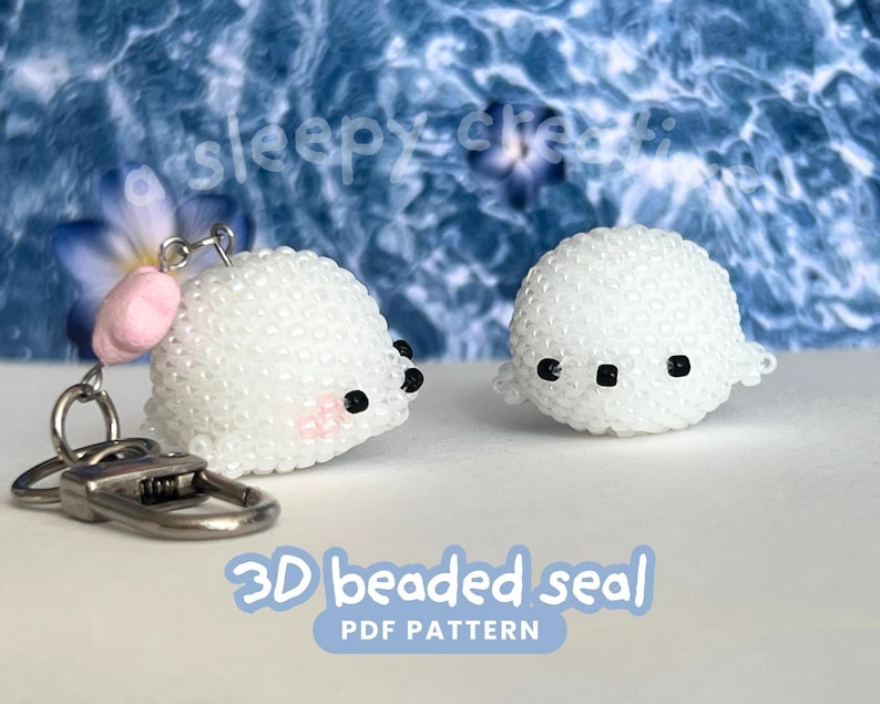 May include: Two white beaded seal figures. One is attached to a keychain with a silver clasp and a pink ear. The other seal is a standalone figure. Both seals have black eyes and are on a light blue background. Text on the image reads "3D beaded seal PDF pattern."