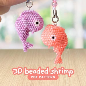 Könnte beinhalten: Zwei 3D-Garnelen-Anhänger aus Perlen, eine hellviolett und eine korallenorange, gefertigt aus kleinen, gleichmäßigen Perlen. Jede Garnele hat ein Auge aus einer weißen und schwarzen Perle sowie einen Metallring. Text: 3D beaded shrimp PDF PATTERN.