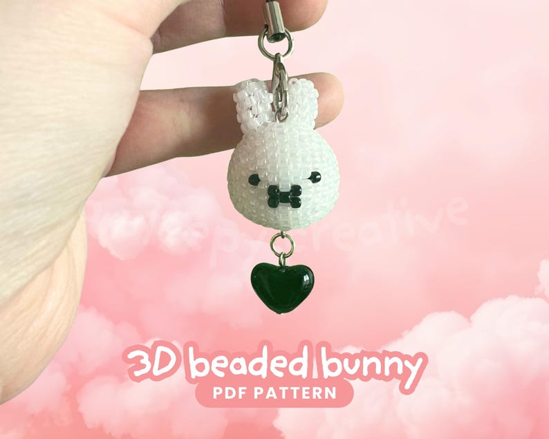 May include: A white beaded bunny charm with a black bow tie and dark green heart pendant. The charm is attached to a silver-colored clasp. Text at the bottom reads "3D beaded bunny PDF PATTERN".