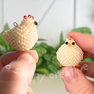 K&ouml;nnte beinhalten: Zwei Perlhuhnfiguren. Eine ist eine Henne mit rotem Kamm und schwarzem Auge, die andere ein K&uuml;ken mit orangefarbenem Schnabel und F&uuml;&szlig;en. Die Figuren bestehen aus kleinen, cremefarbenen Perlen. Der Text "a sleepy creative" ist sichtbar.