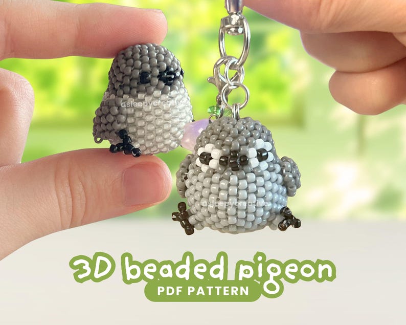 Pu&ograve; includere: Due piccole figure di piccione tridimensionali realizzate con perline grigie, bianche e nere. Un piccione &egrave; attaccato a un portachiavi in metallo argentato, mentre l'altro &egrave; tenuto separatamente. Il testo 3D beaded pigeon PDF PATTERN &egrave; visibile.