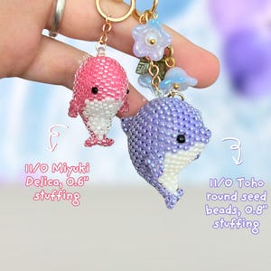 May include: Two beaded dolphin keychains. One is pink and white, the other is purple and white. The pink dolphin is made with 11/0 Miyuki Delica beads and the purple dolphin is made with 11/0 Toho round seed beads. Both have gold-colored key rings.