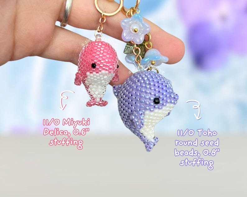 May include: Two beaded dolphin keychains. One is pink and white, the other is purple and white. The pink dolphin is made with 11/0 Miyuki Delica beads and the purple dolphin is made with 11/0 Toho round seed beads. Both have gold-colored key rings.