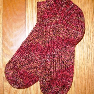 May include: A pair of knitted socks in a red, brown, and gold color scheme. The socks are made with a textured knit and have a ribbed cuff.