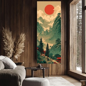 May include: Vertical art print depicting a Japanese landscape with a large red sun, green mountains, and traditional red buildings. The artwork is displayed in a room with wood paneling, a gray sofa, and a round ottoman.