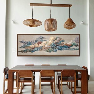 May include: A dining room featuring a long, rectangular wooden table with matching chairs. Above the table hang three pendant lights with woven rattan shades. A large framed painting of colorful clouds adorns the wall.