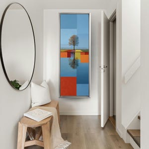 May include: A framed abstract painting featuring a tree reflected in water. The artwork uses a grid of blue, orange, and red squares. The tree is bare, and the sky is a light blue.