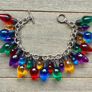 May include: A silver-toned chain bracelet adorned with colorful, light bulb-shaped charms. The bulbs are in various colors, including red, yellow, blue, green, and purple. The bracelet has a toggle clasp.