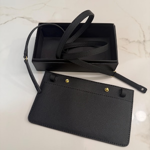 May include: Black leather lanyard with a matching black box. The lanyard has a strap and a cardholder with gold-colored rivets. The cardholder is rectangular and has a textured surface. The box is open and empty.