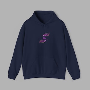 Puede incluir: Sudadera con capucha azul marino con bolsillo delantero y cordón. La sudadera presenta un diseño estilizado en morado y rosa con la palabra "Rise" en el centro.