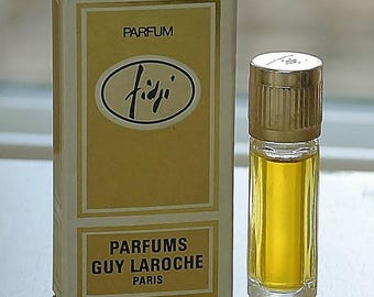May include: A vintage perfume bottle and box. The box is white and gold with the word "PARFUM" at the top and "Fiji" in a script font. The bottle is clear with a gold cap and contains a yellow liquid.