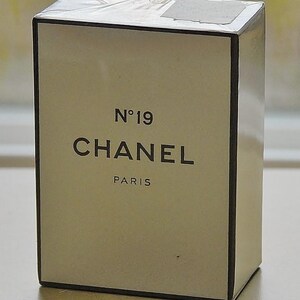 May include: A rectangular box of Chanel No. 19 perfume. The box is off-white with black text that reads "N&deg;19 CHANEL PARIS". The box has a black border and is wrapped in clear plastic.