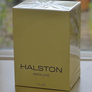 May include: A rectangular box of Halston perfume wrapped in clear plastic. The box is a light beige color with the text HALSTON PERFUME 1 FL. OZ. printed in black on the front. The packaging is sealed and maintains a smooth, clean appearance.