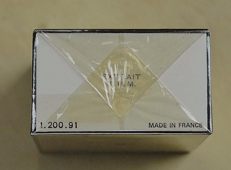 May include: A rectangular box wrapped in clear plastic. The box has white panels and black trim. Text on the box includes "EXTRAIT P.M.", "1.200.91", and "MADE IN FRANCE".