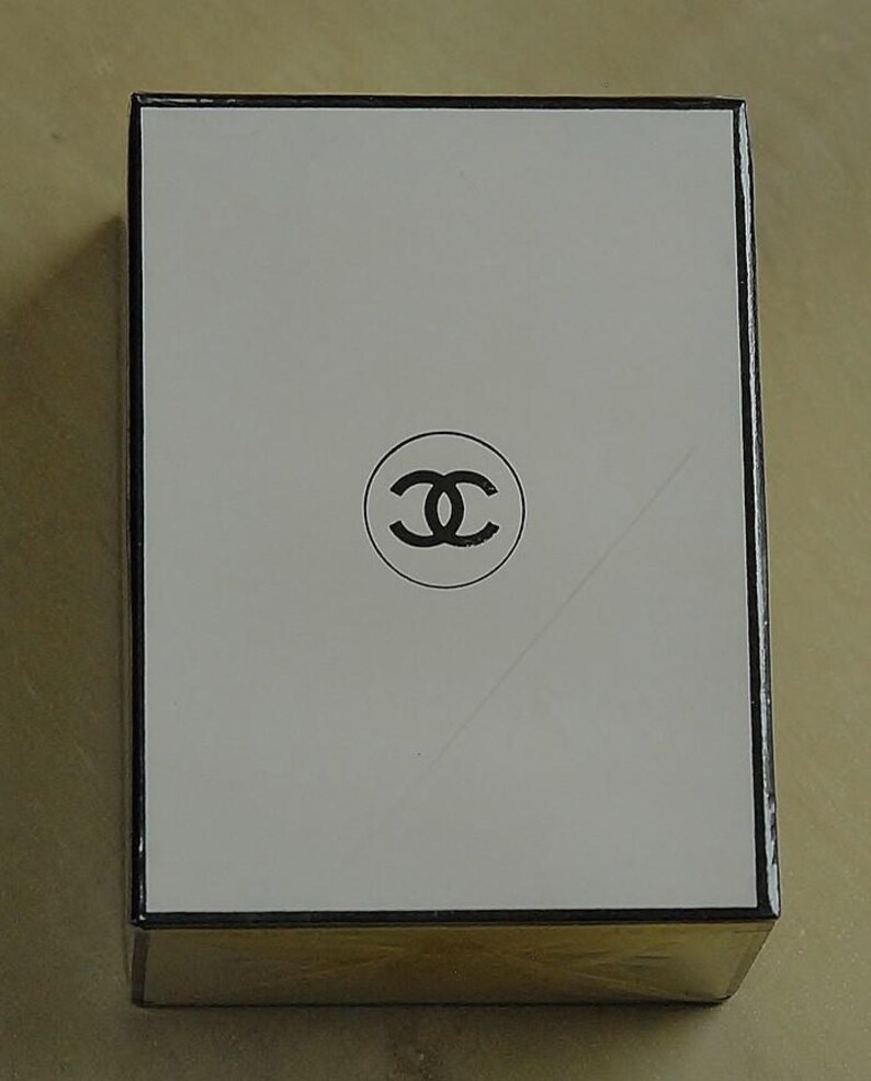 May include: Rectangular white box with a black border and a black double-C logo in the center. The box has a gold-colored base and is likely a product package.