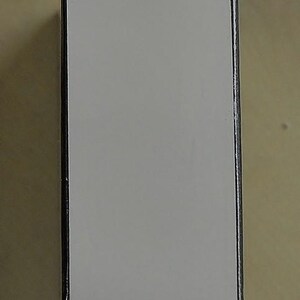 May include: A rectangular box with a white top and gold bottom. The edges are outlined in black. The box is sitting on a light brown surface.