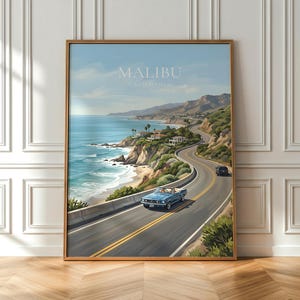 May include: A framed print of a coastal road in Malibu, California. The artwork depicts a winding road along the ocean, with a blue convertible car driving on the road. The sky is blue, and the print is in a wooden frame.