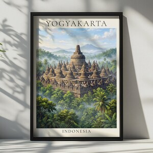 Op de afbeelding: Een ingelijste kunstdruk met de Borobudur-tempel in Yogyakarta, Indonesië. De afbeelding toont de stenen structuur omringd door weelderige groene jungle en bergen onder een blauwe lucht. De tekst YOGYAKARTA en INDONESIA is afgedrukt.