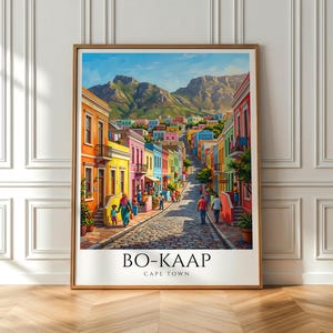 Peut inclure: Une affiche encadrée de Bo-Kaap, Cape Town, représentant une scène de rue colorée avec des bâtiments aux couleurs vives : orange, jaune, rose et bleu. L'œuvre représente une rue pavée avec des gens qui marchent et une montagne en arrière-plan. Le texte "BO-KAAP CAPE TOWN" est en bas.