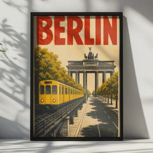 以下が含まれることがあります： 上部に大きな赤い文字でBERLINと書かれた額装された旅行ポスター。高架線路を走る黄色い電車と、その奥に見えるブランデンブルク門、そして道路沿いに並ぶ緑の木々が、明るいベージュの空を背景に描かれたイラストです。