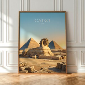 May include: A framed print depicting the Sphinx and pyramids in Egypt. The artwork uses warm colours and has the word "CAIRO" at the top. The print is displayed on a wooden floor against a white wall.