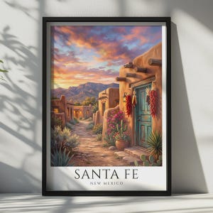 May include: A framed art print depicting a Santa Fe, New Mexico landscape at sunset. The scene features adobe buildings, a turquoise door adorned with red chili ristras, desert flora including cacti, and distant mountains under a vibrant sky.