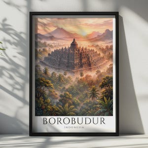 Könnte beinhalten: Ein gerahmter Wandkunstdruck mit einer detaillierten Illustration des Borobudur-Tempels in Indonesien, umgeben von einer üppigen Dschungellandschaft bei Sonnenaufgang mit Bergen im Hintergrund und dem Text BOROBUDUR INDONESIA am unteren Rand.