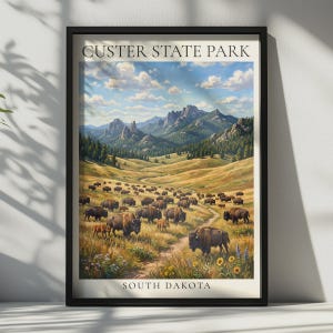 May include: A framed wall art print titled CUSTER STATE PARK SOUTH DAKOTA featuring a landscape painting of a large herd of brown bison grazing in a grassy valley with rolling hills, pine trees, and rocky mountain peaks under a blue sky.
