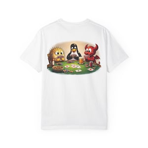 May include: White t-shirt featuring a cartoon illustration of a poker game. The players are a yellow porcupine, a penguin, and a red devil. They are seated around a green poker table with cards, chips, and drinks.