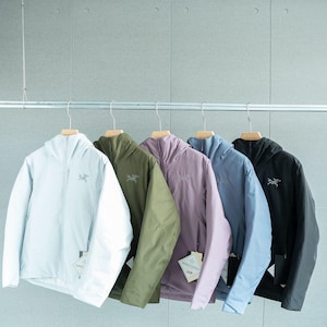 May include: Five hooded jackets in a row, each a different color: light blue, olive green, lavender, periwinkle, and black. Each jacket has a small logo on the chest and is hanging on a wooden hanger. The jackets are displayed against a light gray wall.