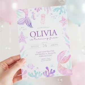 Puede incluir: Una invitación de cumpleaños con temática de sirenas, con el nombre "Olivia" en escritura morada. La invitación presenta ilustraciones de acuarela de colas de sirenas, estrellas de mar y criaturas marinas en colores pastel. El texto dice "Olivia cumple cinco años".