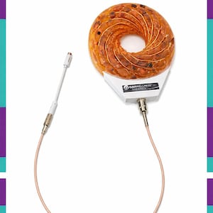 Puede incluir: Un dispositivo en forma de rosquilla, de color naranja-marrón, con una base blanca y un cable color cobre. Un componente blanco en forma de varilla está conectado al dispositivo. El logotipo "GAHWELLNESS" es visible en la base. Fondo blanco con borde turquesa y morado.