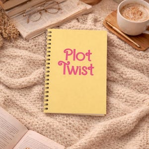 May include: A yellow spiral-bound notebook featuring the text Plot Twist in a bold pink font centered on the front cover. The notebook has a metallic silver wire binding along the left side and a smooth, matte-finish paper cover.